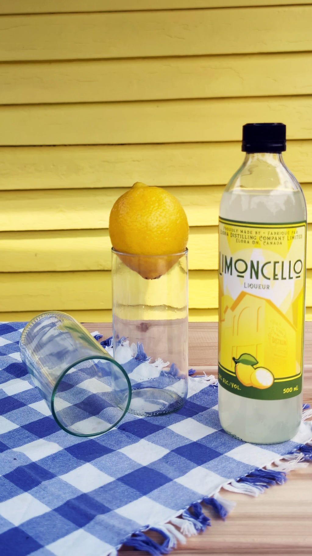 Upcycled drinking glasses with a lemon and a bottle of limoncello on a checkered cloth.