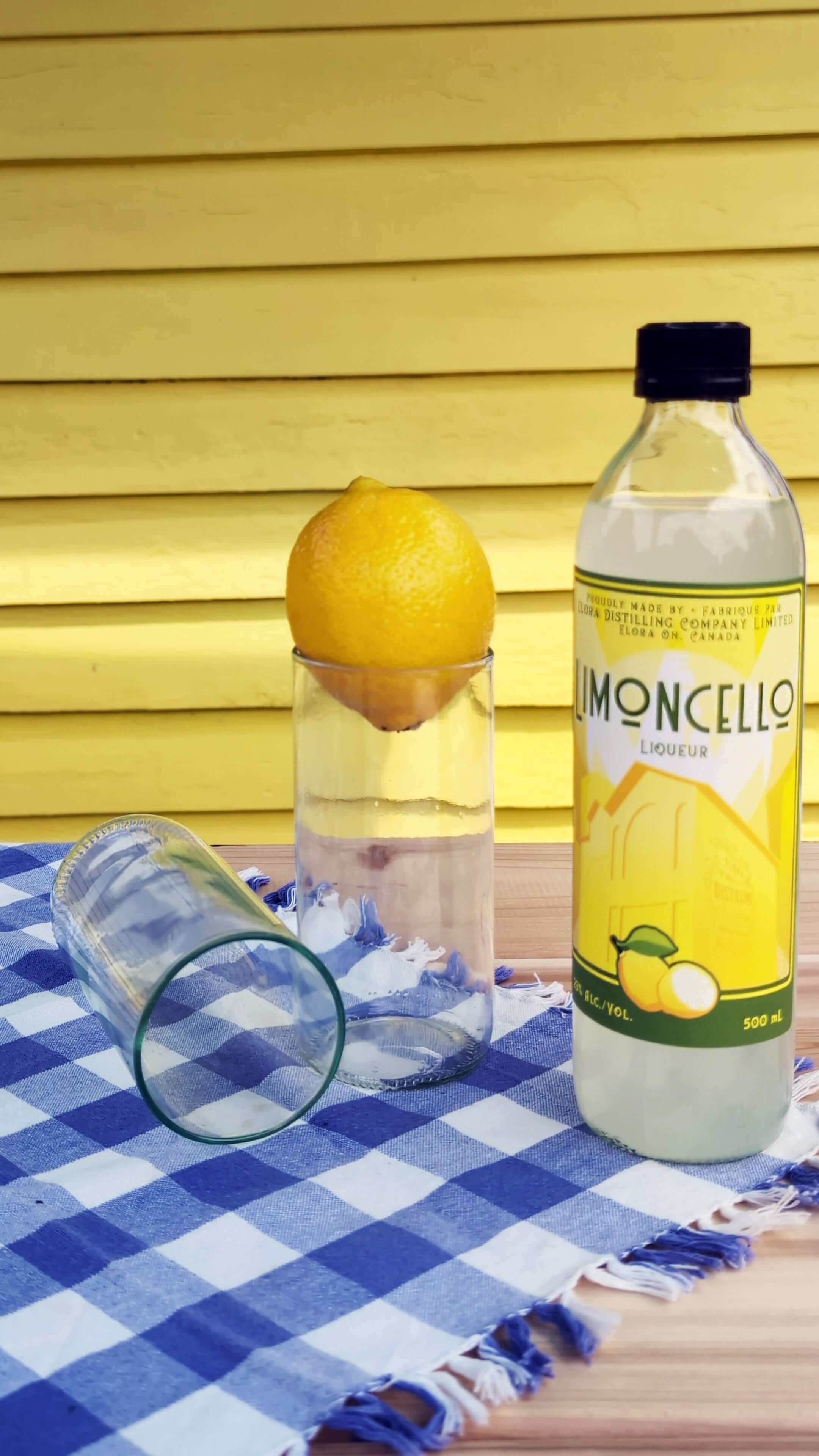 Upcycled drinking glasses with a lemon and a bottle of limoncello on a checkered cloth.