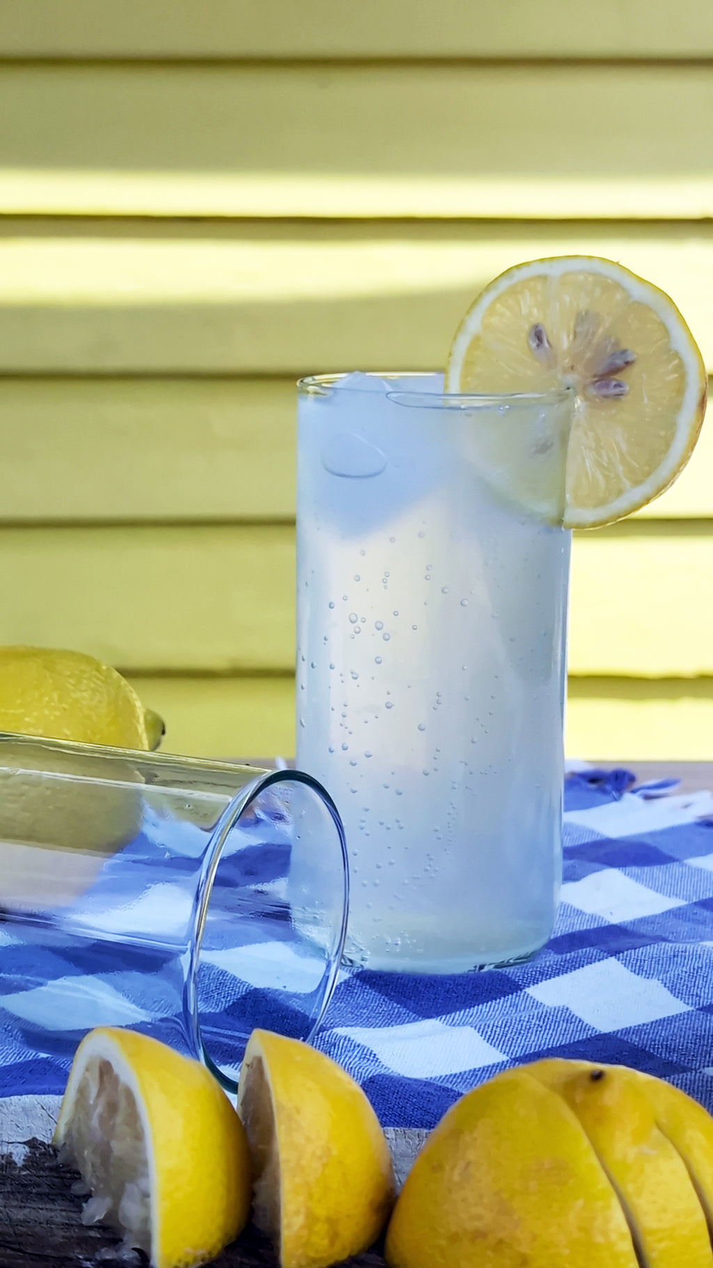 Upcycled drinking glasses filled with sparkling water and lemon slice on a blue checkered tablecloth.