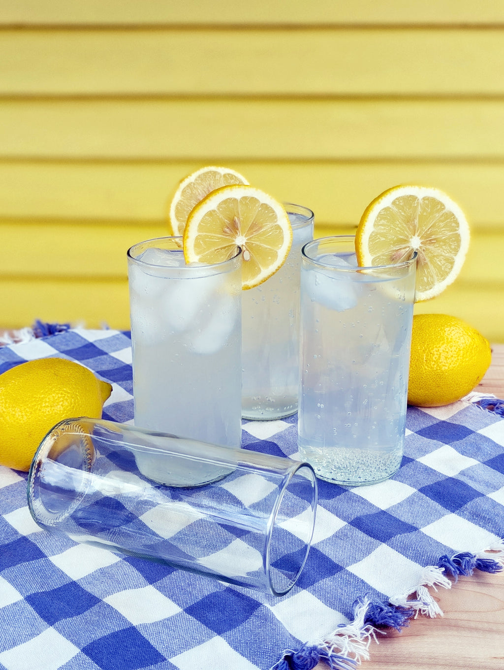 Upcycled drinking glasses filled with lemonade, garnished with lemon slices on a checkered cloth.